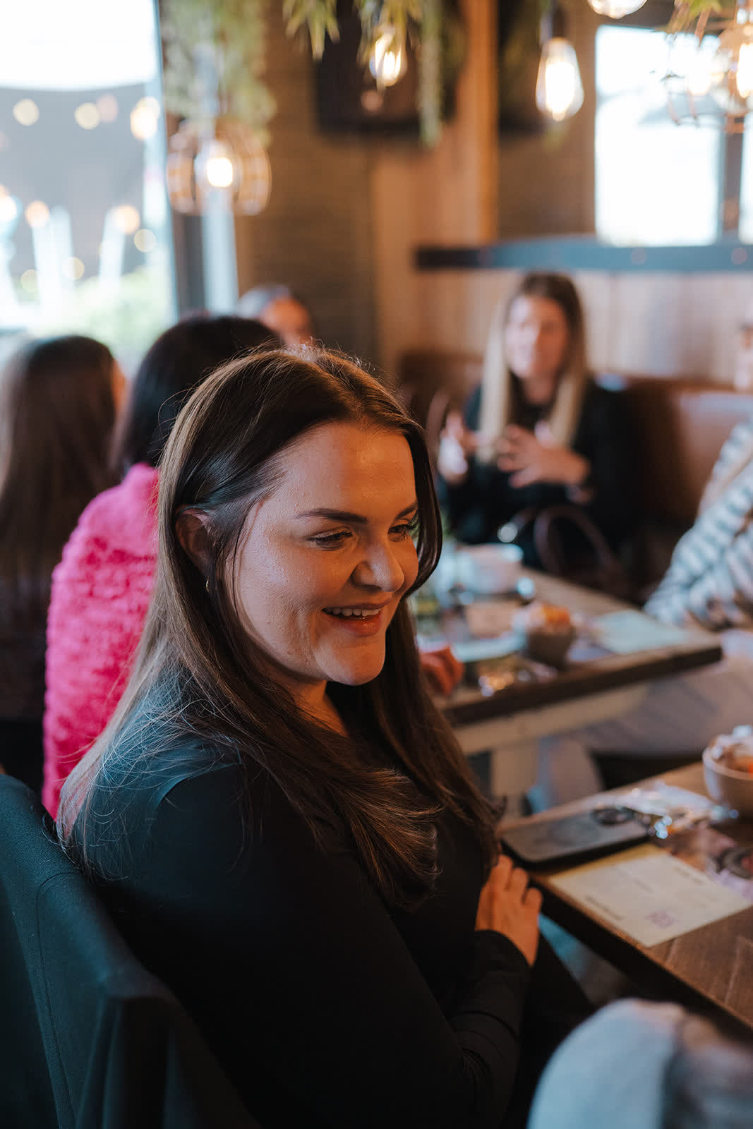 A woman smiling at a catch-up table with others chatting behind her